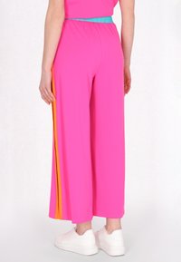 Roze wijde broek met een elastische tailleband, voorzien van oranje zijkanten en een gladde textuur. Gecombineerd met witte sneakers.