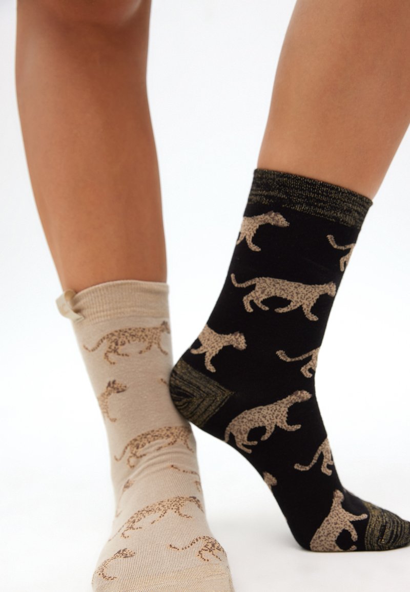 Beige och svarta strumpor med leopardmönster; den beiga strumpan har en ljusbrun bas med ett brunt mönster, medan den svarta strumpan har en mörk ton med ljusa mönster.