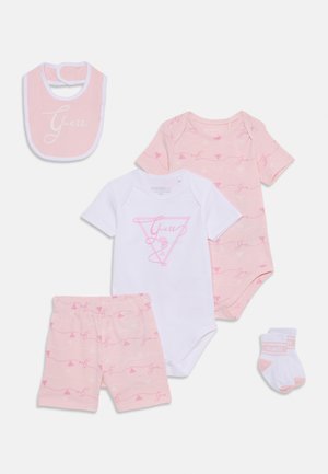 Set di abbigliamento per bambini composto da cinque pezzi: un bavaglino rosa, un body bianco, una maglietta rosa a fantasia, pantaloni corti coordinati e calzini con il logo "Guess", realizzati in materiali morbidi.