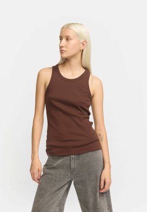Débardeur marron avec un col rond et sans manches, fabriqué en tissu lisse. Porté avec un pantalon large gris.
