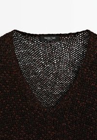 Vêtement à col en V en maille ajourée marron foncé avec une étiquette Massimo Dutti à l'intérieur du col, montrant la texture et le motif de tricot détaillé.