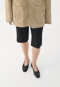 Beige velúr dzseki két elülső zsebbel, fekete, térd fölé érő rövidnadrággal és fekete, négyzet orrú lapos cipővel párosítva. Simább textúra és egyszerű dizájn.