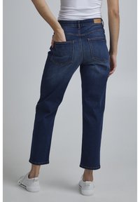 Mörkblå denimjeans med hög midja, rak passform och två bakfickor. Midjebandet har en diskret läderpatchdetalj.