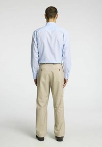 Svijetloplava prugasta košulja i bež krojene hlače, s detaljima na leđima i dva stražnja džepa, prikazano odostraga.