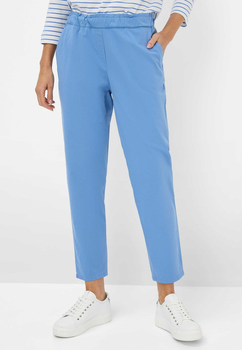 Hellblaue Hose mit lockerer Passform, elastischem Bund, Seitentaschen und Bündchen, die am Knöchel enger werden. Getragen mit weißen Sneakern.