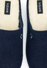 Navy blue felt slippers with cream fleece lining, featuring a simple design and subtle embroidered detail on the sides. Brand label visible.