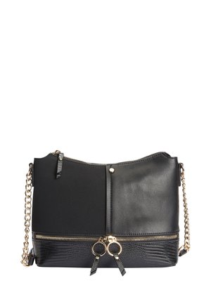 Sac à main en cuir noir avec bandoulière chaîne dorée, fermeture éclair dorée et deux tirettes en forme d’anneau doré sur un panneau inférieur texturé.