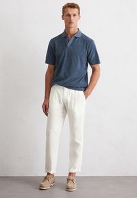 Donkerblauwe heren polo met korte mouwen, gecombineerd met witte linnen broeken en lichtbeige schoenen. Gladde stofstructuur, casual pasvorm.