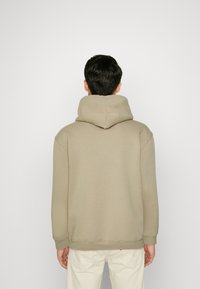 Sudadera con capucha en beige, confeccionada con tela suave. Presenta un ajuste relajado, puños y dobladillo acanalados. Diseño liso, sin patrones ni detalles visibles.