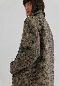 Brun tweedfrakke med krave, tekstureret stof og synlige syninger. Har en afslappet pasform og sidelommer.