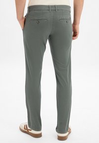 Jasnozielone spodnie wykonane z gładkiego materiału, wyposażone w dwie tylne kieszenie z zapięciami na guziki, w stylu prostych nogawek.