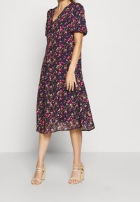 Květinové midi šaty s tmavě modrým pozadím, krátkými nabíranými rukávy, výstřihem do V a splývavým lemem, zdobené růžovými a žlutými květinovými vzory.