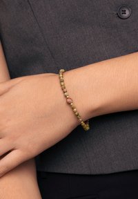 Pulsera de cuentas con piedras verdes, rosas y doradas, ensartadas en un elástico. El diseño es sencillo, ajustándose estrechamente alrededor de la muñeca.