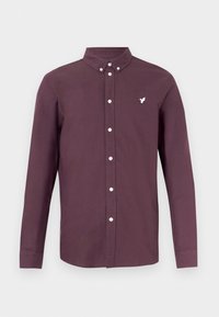 Chemise à manches longues boutonnée de couleur violet foncé avec un col boutonné et un petit logo oiseau blanc sur la poitrine gauche.