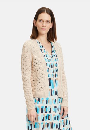 Hellbeige gestrickte Strickjacke mit Lochmuster, gerippten Bündchen und lockerer Passform, kombiniert mit einem multicolorierten abstrakten Druckkleid.