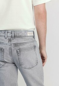 Light grey denim jeans with a slim fit, featuring two back pockets and a label that reads "hessnatur NATURDENIM."