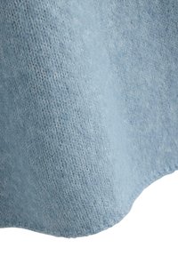 Lähikuva vaaleansinisestä kudotusta kankaasta, jolla on pehmeä, pörröinen tekstuuri ja näkyvä neulekuvio.