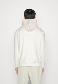 Sudadera de color claro con una gran capucha suave. Cuenta con un ajuste relajado, puños acanalados y un logotipo tenue estampado en la parte posterior.