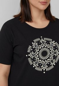 Zwart T-shirt met korte mouwen, voorzien van een cirkelpatroon in wit en grijs op de voorkant. Soepele katoenstof.