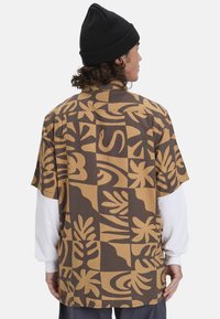 Korte mouwen shirt met een bruine basis en grote tan abstracte bloemenpatronen, gemaakt van een lichte, textuurstof.