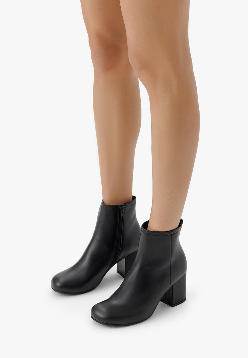 Botine negre din piele cu un finisaj neted, vârfuri rotunde și un toc pătrat de 10 cm; au un fermoar pe lateral pentru a fi ușor de purtat.