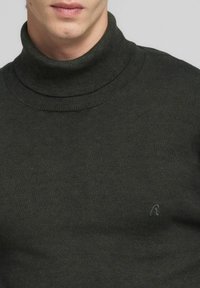 Suéter de cuello alto verde oscuro en un tejido suave y acanalado. Presenta un diseño ceñido con un logo sutil en el pecho.