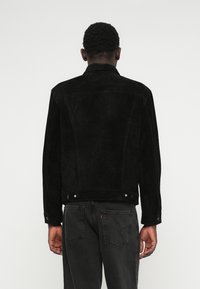 Μαύρο σουέτ μπουφάν με κλασικό γιακά, πίσω ρέλι και κουμπιά πατητού, σε συνδυασμό με σκούρα τζιν. Διαθέτει υφή και δομημένη σιλουέτα.