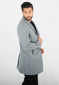 Manteau en mélange de laine gris avec col à revers, fermeture à un bouton et poches latérales, présentant une coupe ajustée et une texture lisse.