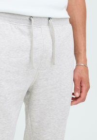 Lichtgrijze sweatpants met een trekkoord in de taille, met een zachte textuur en een aansluitend ontwerp. Accenten van metalen oogjes.