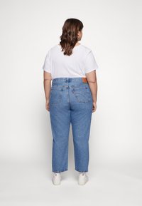 Jean en denim bleu taille haute avec une coupe décontractée, cinq poches, couture visible et un patch en cuir marron à la taille arrière.