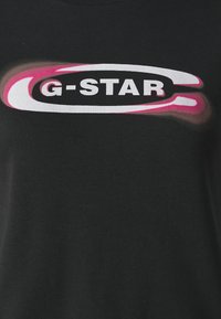 Černé bavlněné tričko s velkým logem G-STAR v bílé a růžové barvě, s hladkou texturou a krátkými rukávy.
