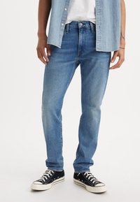 Jean en denim bleu clair avec une coupe droite, design à cinq poches et fermeture à bouton, associés à des baskets montantes noires.