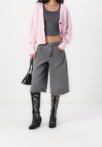 Růžový pletený kardigan, šedý krátký top, šedé široké džíny se staženým střihem, černé vzorované vysoké boty ke kolenům a malá černá kabelka.