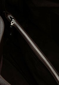 Interno di una borsa in pelle marrone con una cerniera argentata, texture a contrasto e foderatura morbida in tonalità scure. Dettaglio di cuciture ben visibile.