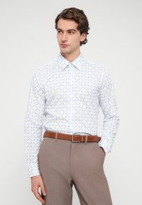 Λευκό πουκάμισο με μακριά μανίκια και ανοιχτό μπλε λουλουδάτο σχέδιο, γιακά με κουμπιά και λείο ύφασμα, συνδυασμένο με καφέ ζώνη και γκρι παντελόνι.