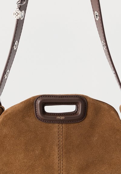 Καφέ τσάντα από σουέτ με δερμάτινο πάνω χερούλι, ασημένιες μεταλλικές λεπτομέρειες και ανάγλυφο λογότυπο σε αντίθεση. Ομαλή υφή σε όλη την επιφάνεια.