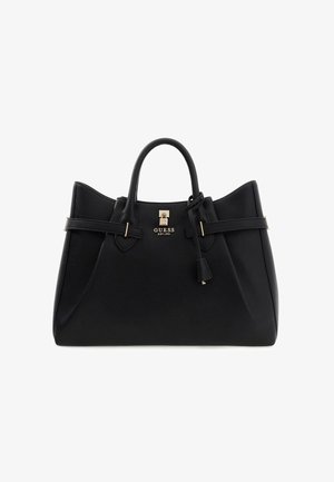 Sac à main Guess en cuir noir avec deux poignées, brides latérales, détail de verrou doré et une étiquette en cuir suspendue sur fond blanc.