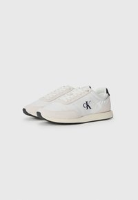 Witte sportieve sneakers met suède en stoffen panelen, voorzien van een zwarte rubberen zool en geborduurd "cK" logo aan de zijkant.