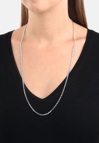 Silver kedja med ovala länkar, som bärs över en svart V-halsad tröja. Kedjans yta är slät och glänsande, vilket skapar en reflekterande effekt.