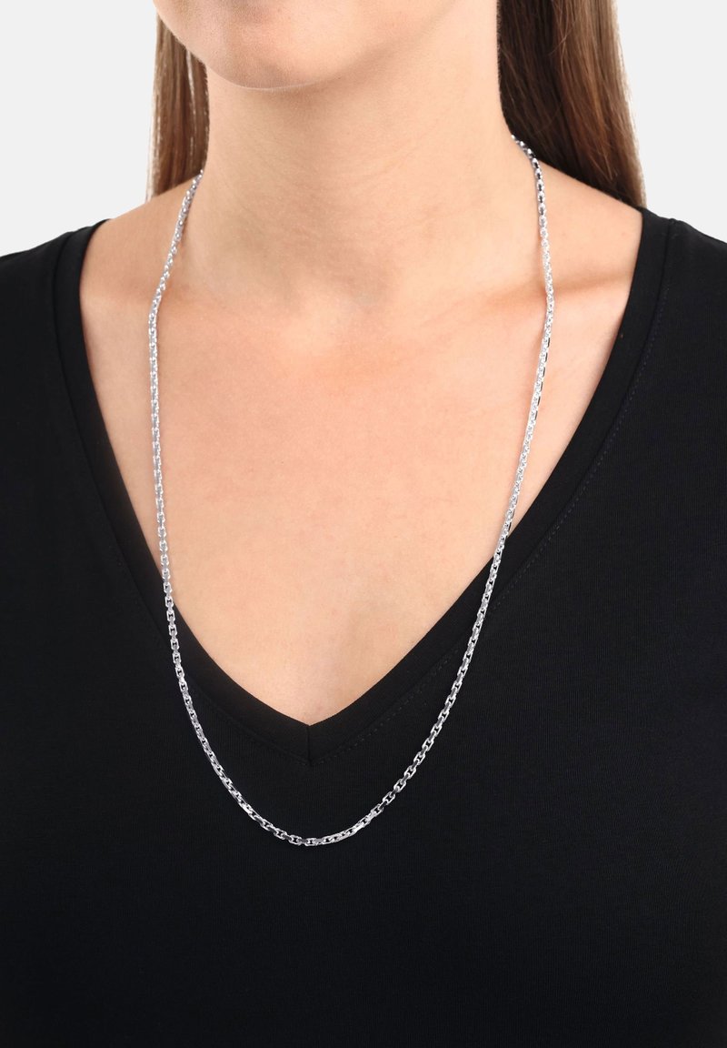 Silver kedja med ovala länkar, som bärs över en svart V-halsad tröja. Kedjans yta är slät och glänsande, vilket skapar en reflekterande effekt.