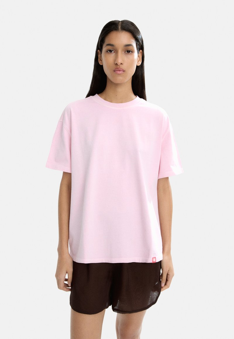 Jasnoróżowa bawełniana koszulka z krótkim rękawem, okrągłym dekoltem i luźnym krojem. Posiada małą metkę z logo przy dolnym brzegu.