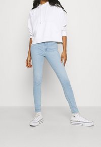 Jeans skinny de color azul claro combinados con un hoodie corto blanco. El conjunto se complementa con zapatillas altas blancas.