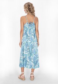 Rochie maxi fără mâneci, de culoare albastru deschis, cu un model paisley, detaliu cu fundă la spate și material fluid. Asortată cu sandale espadrile bej cu curea.