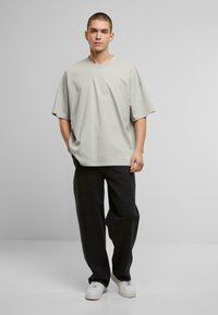 Hellgraues, oversized T-Shirt aus Baumwollmischung, mit kurzen Ärmeln und Rundhalsausschnitt. Kombiniert mit schwarzen weiten Hosen und weißen Sneakers.