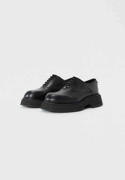 Black leather lace-up shoes with rounded toes and thick rubber soles, featuring a smooth finish and minimalist design.