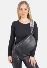 Schwarze Ledertasche im Sling-Design mit geschwungener Form und strukturiertem Finish. Verfügt über einen gemusterten Träger und einen Reißverschluss, der quer über den Oberkörper getragen wird.