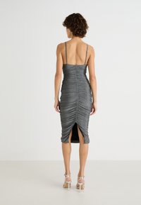 Robe midi grise ajustée avec des détails froncés, fines bretelles réglables et fente sur le côté. Fabriquée en tissu métallique texturé.