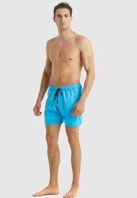 Modré plavky s elastickým pasem, stahovací šňůrkou a volným střihem. Hladká látka bez viditelných vzorů nebo ozdob.