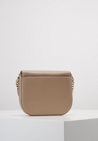 Beige nahkainen crossbody-laukku, joka on pyöreän muotoinen, kultaketjuhihnalla ja läppäkiinnityksellä. Sujuva pinta, jossa on minimalisiä muotoiluelementtejä.