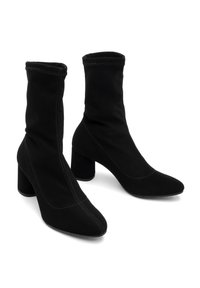 Bottines noires en tissu doux avec une coupe ajustée, des talons carrés et des détails de couture visibles sur les côtés et au niveau des orteils.